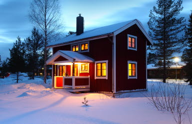 Ett rött trähus med vita knutar står upplyst en mörk vinterkväll.