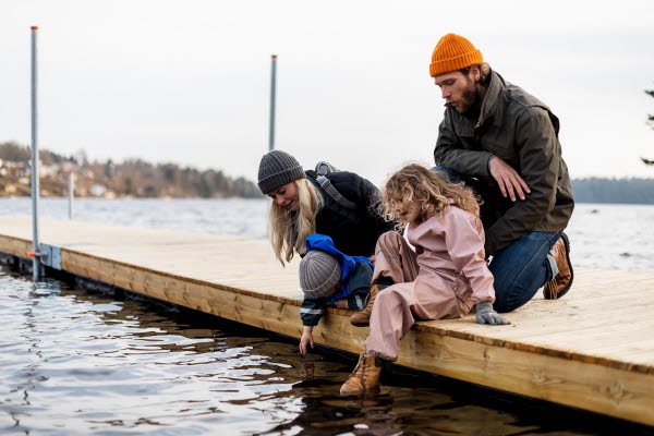 En mamma, pappa, son och dotter sitter på en brygga vid vattnet.