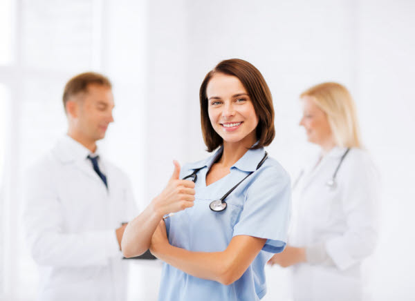 Sköterska som håller upp en tumme och ler mot kameran.