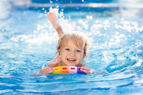 Ett litet barn simmar skrattandes med hjälp av en flytkudde