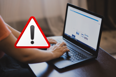 En person sitter och skriver på en dator. På bilden finns en röd triangel med ett svart utropstecken.