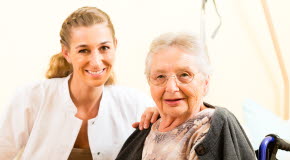 Bilden visar en vårdpersonal med en äldre kvinna i rullstol