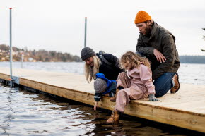 En mamma, pappa, son och dotter sitter på en brygga vid vattnet