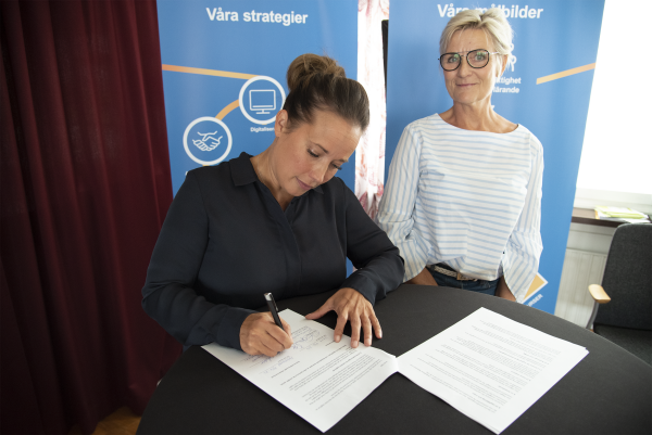 Två kvinnor skriver under ett avtal om Gemensam familjehemsorganisation.