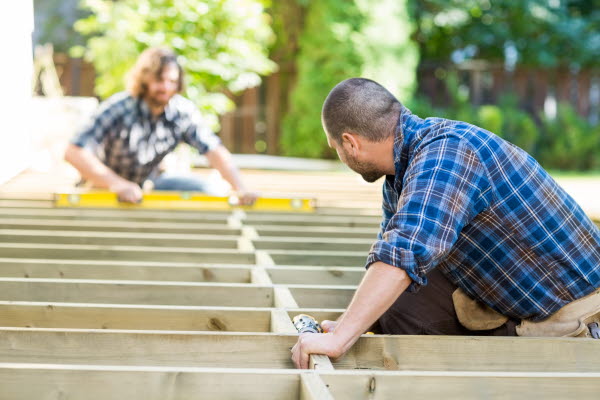 Två män bygger på en altan under sommaren.