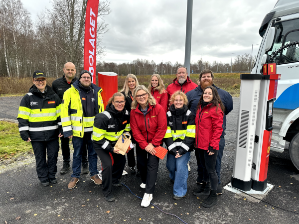 Qstars vd Maria Hadd (i röd jacka i mitten längst fram) omgiven av medarbetare från huvud- och regionkontor. Gruppen på 11 personer står bredvid en laddstolpe.