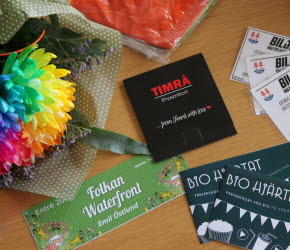 På ett bord ligger en regnbågsfärgad blombukett, biobiljetter, entrébiljett till Folkan Waterfront, presentkort och matchbiljetter till Timrå IK.