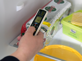 En hand håller en termometer som mäter temperaturen på en leverpastej inuti ett kylskåp.